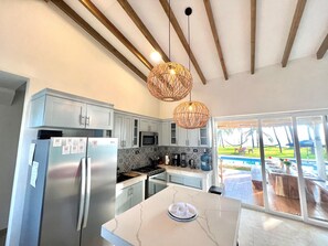 Cozinha moderna com eletrodomésticos de aço inoxidável, bancada de mármore e vista para uma piscina.