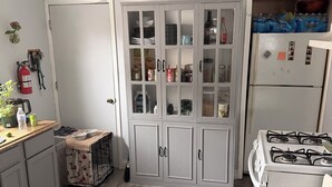 Een keuken met een witte koelkast, een gasfornuis, een kast met glazen deuren, en een bord met de tekst 'gather' erboven.