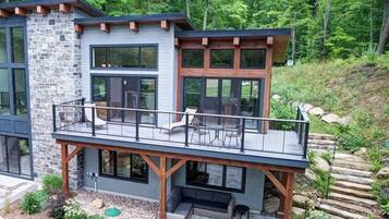 Une maison moderne à deux étages, dotée d’un balcon, d’une façade en pierre et offrant une vue sur une zone boisée.