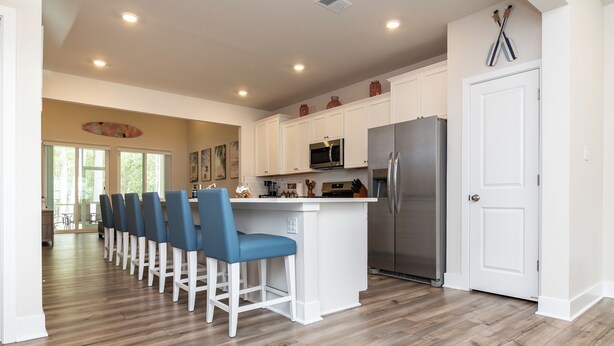 Una cocina moderna con armarios blancos, un refrigerador de acero inoxidable y una zona de bar con sillas azules.