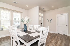 A dining room with a rectangular table, white chairs, a vase with flowers, and a door with a lock. - Welcoming 4BR Villa with Pool in Charming Frankford (Frankford)