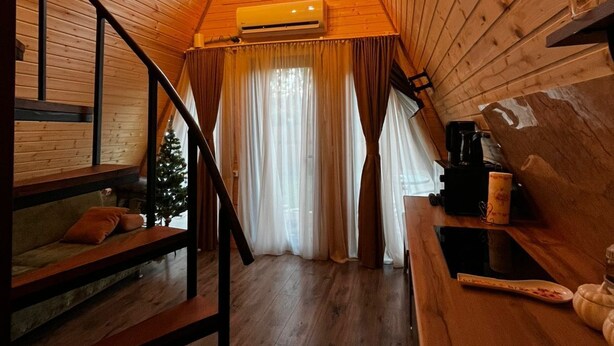 Un intérieur en bois avec un escalier, un petit coin cuisine et une fenêtre avec des rideaux.