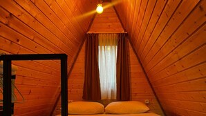 Une chambre mansardée chaleureuse, avec un plafond en pente, un lit simple avec une literie blanche et une fenêtre avec des rideaux.