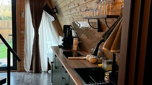 Un intérieur en bois comprenant un coin cuisine, une fenêtre avec des rideaux et un chat qui se promène.