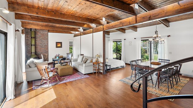 A spacious living area with a high ceiling, wooden beams, a fireplace, and a dining area with a staircase. - Spacious Retreat Near Boston with AC, Roku, Deck, BBQ Grill + Pet Friendly! (Framingham)
