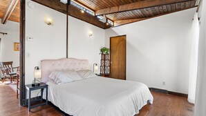 A bedroom with a large bed, wooden beams, a nightstand, a wall-mounted light, and a door. - Spacious Retreat Near Boston with AC, Roku, Deck, BBQ Grill + Pet Friendly! (Framingham)