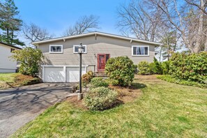 A single-story house with a garage, a front door, and a small front yard with bushes and a street lamp. - Spacious Retreat Near Boston with AC, Roku, Deck, BBQ Grill + Pet Friendly! (Framingham)
