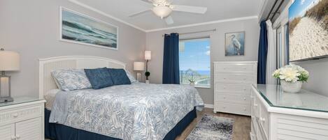 A bedroom with a bed, a ceiling fan, a window with curtains, a dresser, and a wall-mounted TV.