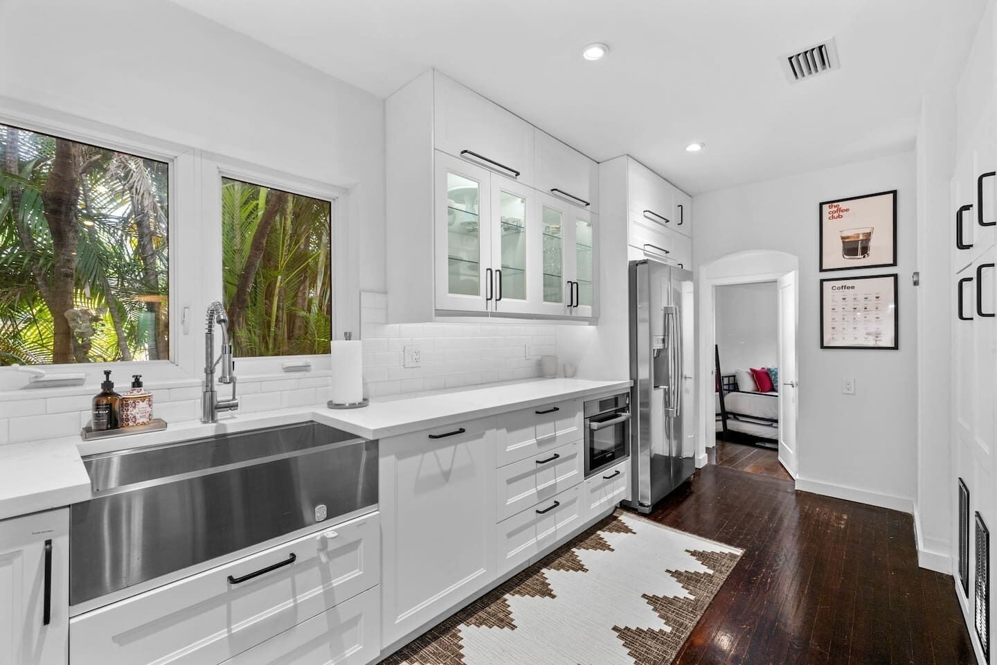 A modern kitchen with white cabinetry, stainless steel appliances, and a large window with a view of greenery.