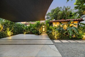 Un chemin menant à un bâtiment doté d’un toit en tuiles, entouré d’une végétation luxuriante.