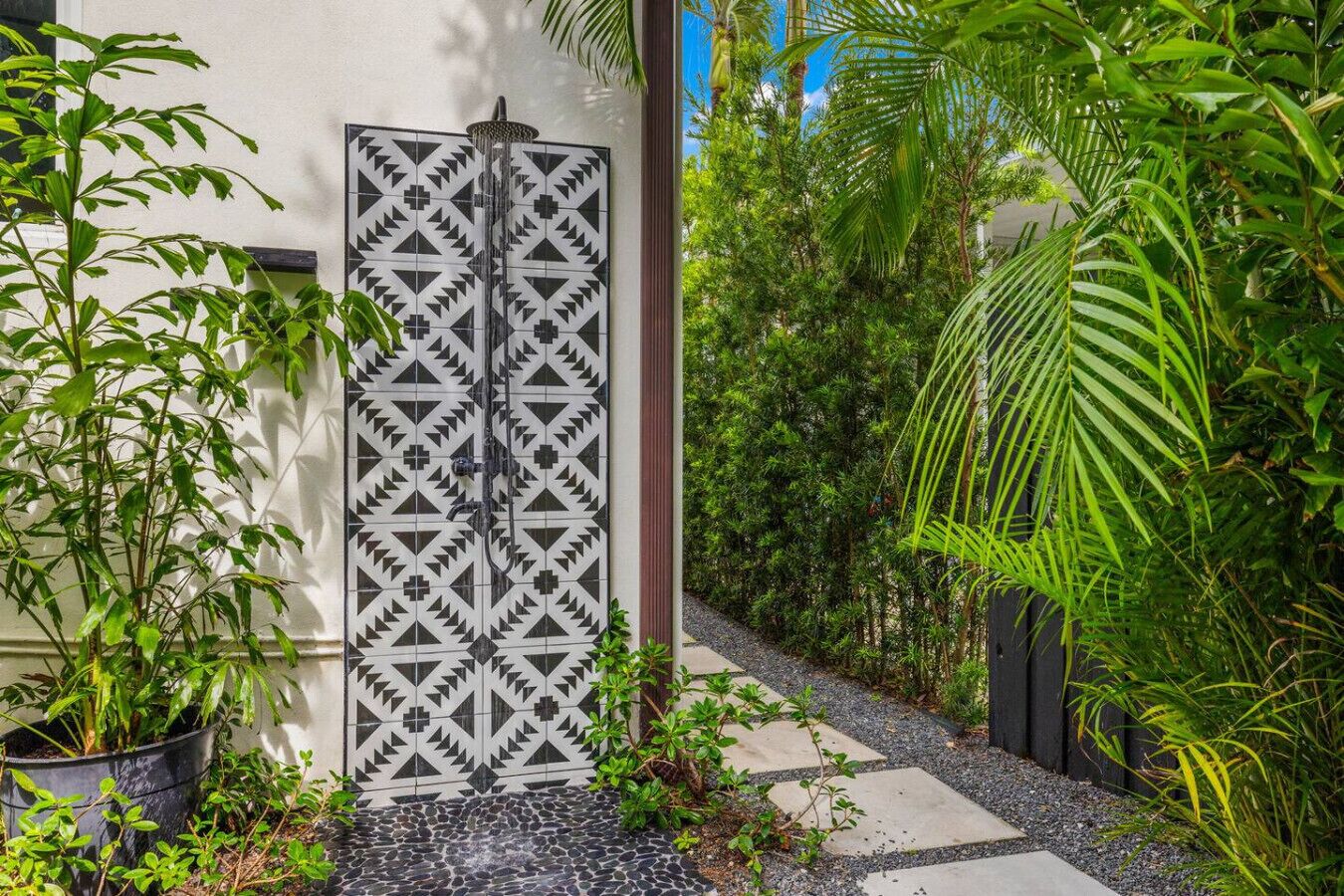 A garden pathway leading to a door with a geometric tile design, surrounded by lush greenery and potted plants.