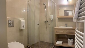 Un bany amb dutxa amb envàs de vidre, un vàter, un lavabo amb mirall i un escurapulides.