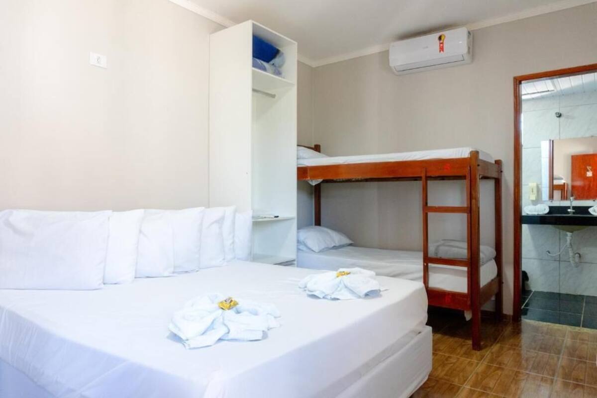 A room with a bunk bed, a single bed, a wardrobe, a mirror, and a bathroom with a sink.