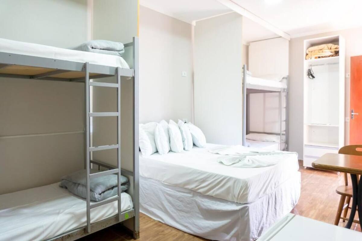 A dormitory room with bunk beds, a single bed, a wooden table, and a wardrobe.