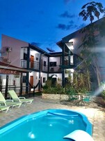 Un edificio de varios pisos con piscina, mobiliario de exterior y jardín.
