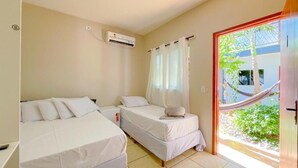 A room with two beds, a window with curtains, an air conditioning unit, and a view of greenery outside. - Pousada papaya (Bonito)