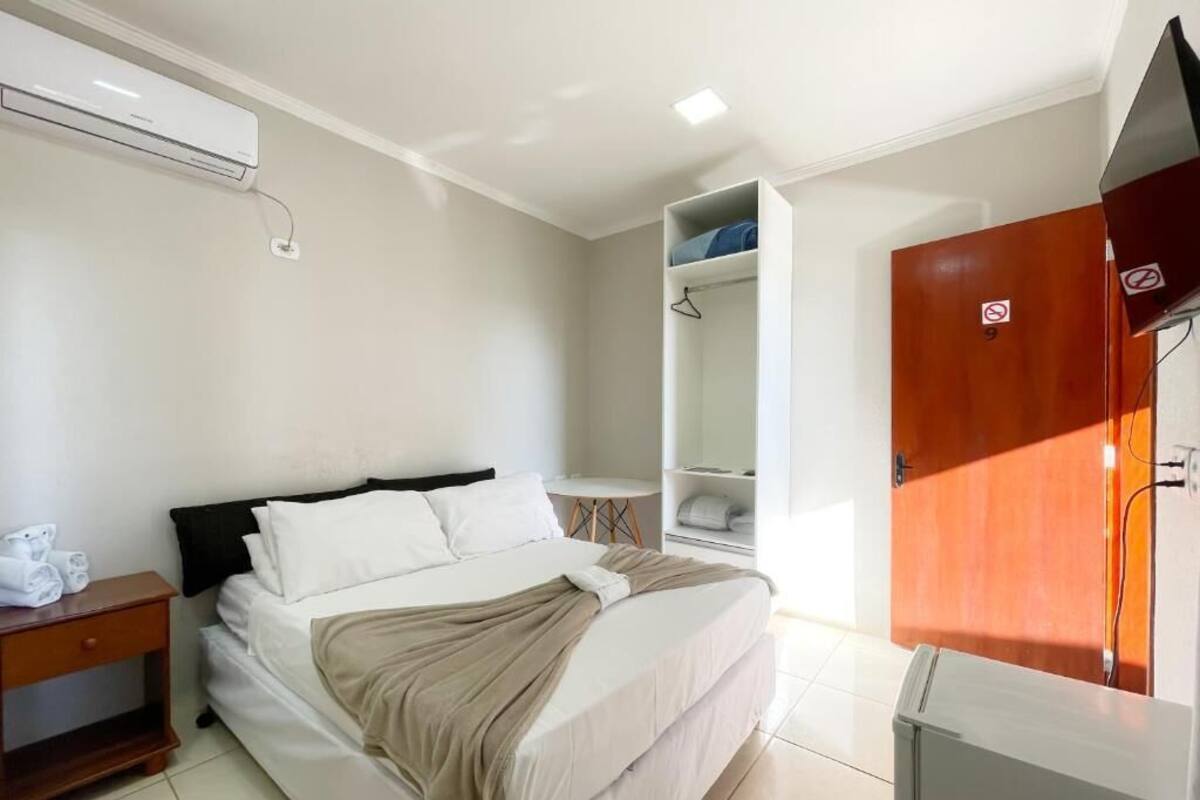 A bedroom with a bed, a wardrobe, a desk, and a hanging shelf.