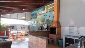 A kitchen with a brick oven, a dining area with a table and chairs, and a mural on the wall. - Pousada papaya (Bonito)