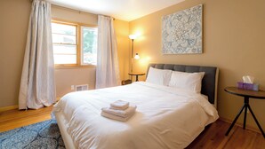 Ein Hotelzimmer mit einem großen Bett, einem Nachttisch, einer Lampe, einem Fenster mit Vorhängen und einem Wandbild.