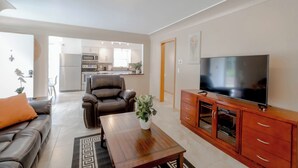 Ein modernes Wohnzimmer mit einer Couch, einem Couchtisch, einem Fernseher und einer Küche im Hintergrund.