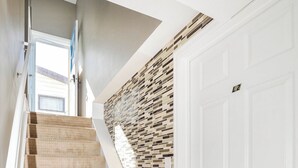Eine Treppe mit beigem Teppich führt zu einer weißen Tür, eine Wand mit Mosaikmuster und eine moderne Decke.
