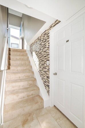 A staircase with beige carpet leading to a white door, a wall with a mosaic pattern, and a modern ceiling. - 907- Walk to Mayo St Mary Hospital 4 bed/2 bath 2 living rooms, Laundary/Parking (Rochester)