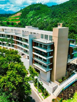 A modern multi-story building with a flat roof, surrounded by lush greenery and hills. - hihome - Reserva Granja Brasil (Petrópolis)