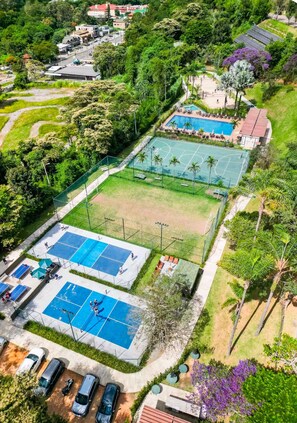 Luchtbeeld van een sportcomplex met meerdere tennisbanen, een zwembad en een parkeerplaats.
