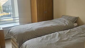 A bedroom with two beds, a wooden wardrobe, a window with a view, and a hanging light fixture.