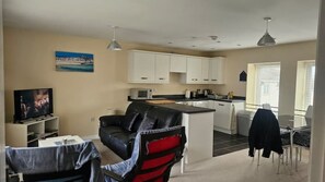 Un espacio habitable compacto con sofá, televisión, zona de cocina y mesa de comedor.
