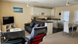 Ett kompakt bostadsutrymme med en soffa, TV, ett litet kök, en matplats och en tavla på väggen.