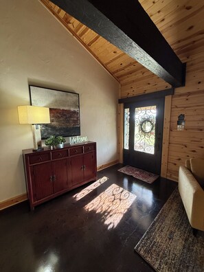 Interior de madera con piso de madera oscura, un armario con un letrero de 'Welcome', una lámpara y una puerta con un ventanal decorativo.