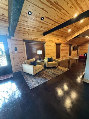 Interior de una cabaña de madera con dos sofás, una lámpara y una alfombra.