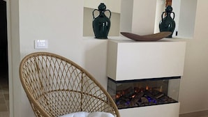 A wicker chair with a cushion, a white fireplace with a glass front, and two dark vases on shelves above it. - Il Villino - Luxury Country House, a luxury retreat between nature and tradition (Puglia)