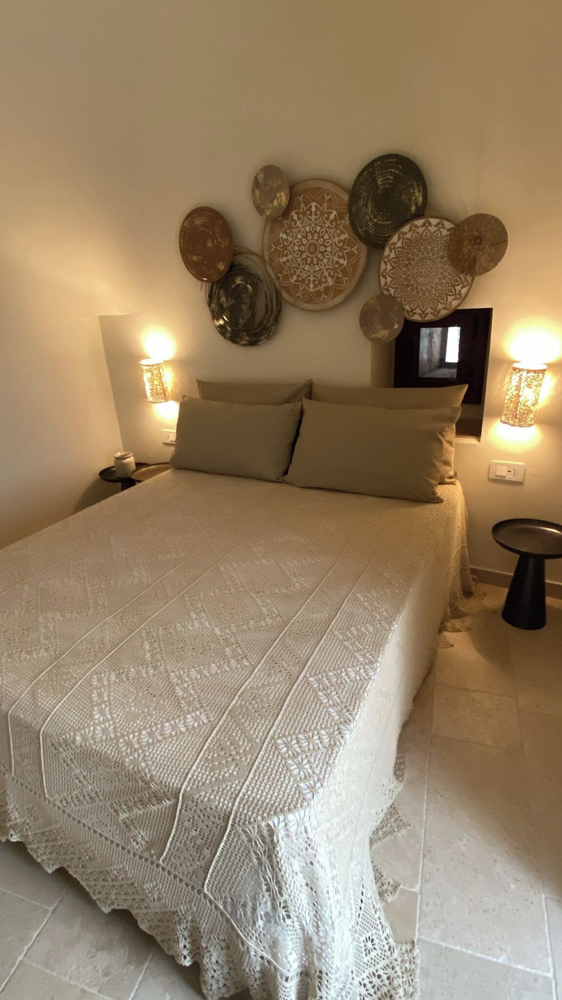 Una cama con cubrecolcha de encaje blanco, dos almohadas, un televisor montado en la pared y platos decorativos sobre la cama.