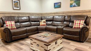 Ein braunes, ledernes Ecksofa mit karierten Kissen, ein Couchtisch aus Holz mit Schachbrett und ein Holzschrank mit japanischen Schriftzeichen.