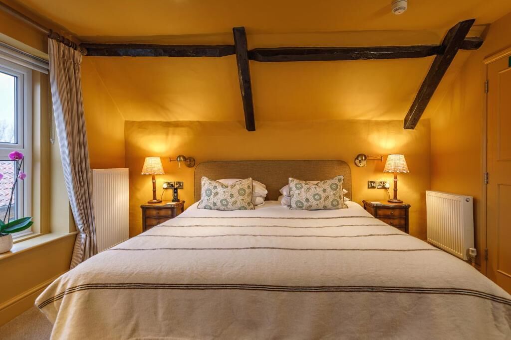 A bedroom with a bed, two bedside lamps, a window with curtains, and a radiator.
