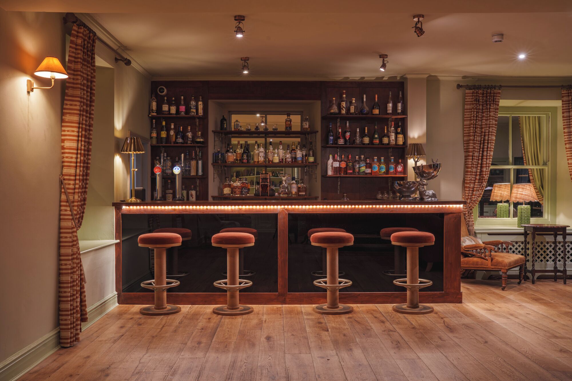 Un espace bar avec un plancher en bois, des tabourets de bar et une variété de bouteilles exposées sur des étagères.