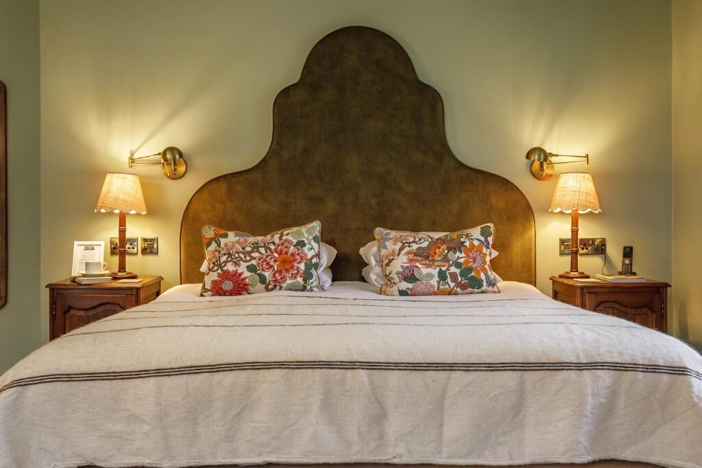 Una cama con cabecera de madera, dos lámparas de noche y almohadas estampadas con motivos florales.