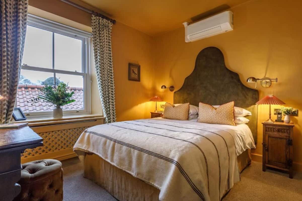 Quarto com cama grande, janela com cortinas, mesa de cabeceira com abajur e ar-condicionado fixado na parede.