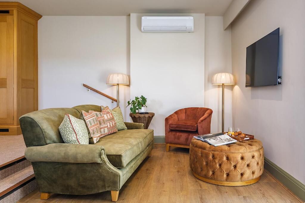A living room with a sofa, armchair, ottoman, lamp, and a flat-screen TV.