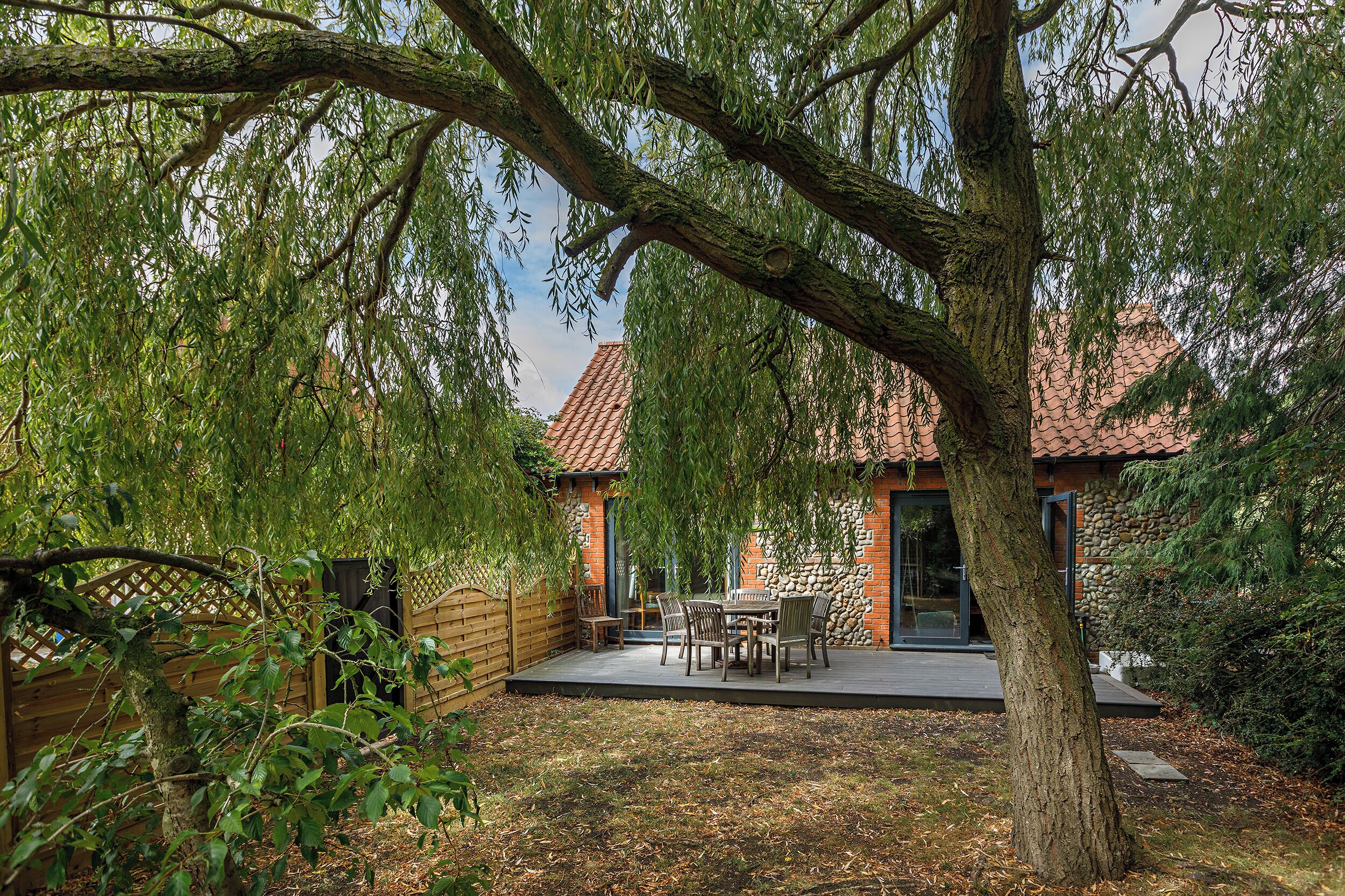 A patio with outdoor furniture, a wooden fence, and a tree providing shade.