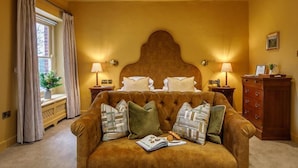 A bedroom with a large bed, two bedside lamps, a wooden dresser, and a window with curtains.