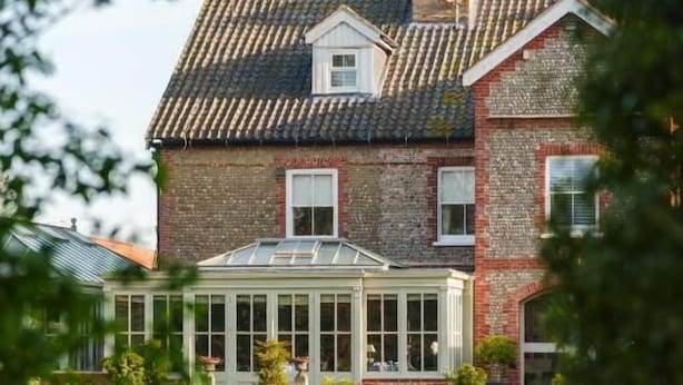 A large brick house with a conservatory and a pond in the foreground.