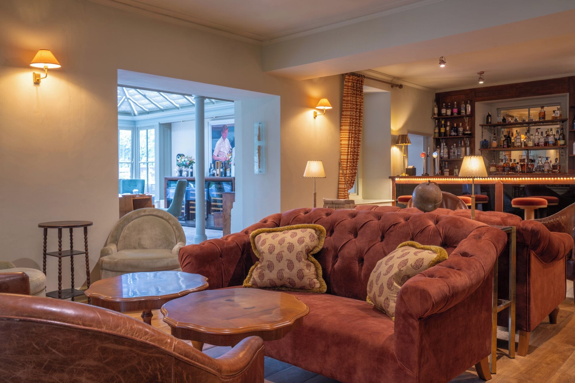 A cozy living room with a plush red sofa, a wooden coffee table, and a bar area with shelves of bottles.