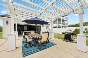 A covered patio with a table and chairs, a grill, and a pergola structure. - Spacious 5-bedroom house in charming Destin with AC (Destin)