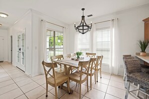 A dining area with a round table, wooden chairs, a chandelier, and large windows with white curtains. - Spacious 5-bedroom house in charming Destin with AC (Destin)