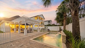 Una piscina con una pérgola, una casa de dos pisos y una valla blanca.