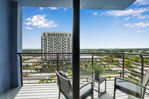 A balcony with a view of a tall building, a potted plant, and a chair. - Modern Studio | Pool View | Downtown Doral' Heart (Doral)
