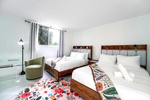 Habitación de hotel con dos camas, una silla, una lámpara y un ventanal con cortinas.